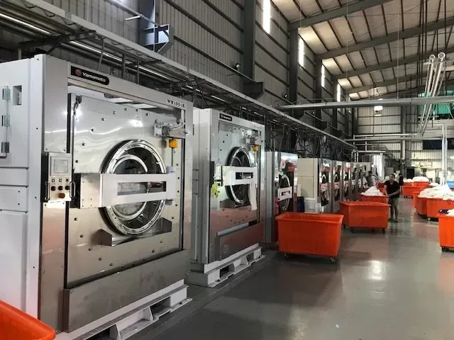 Industrial laundry wash aisle with a tunnel washer and mixed-brand washer-extractors