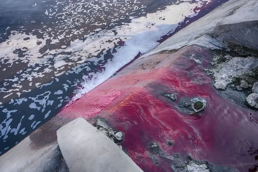 Bright red industrial wastewater flowing into a contaminated water body